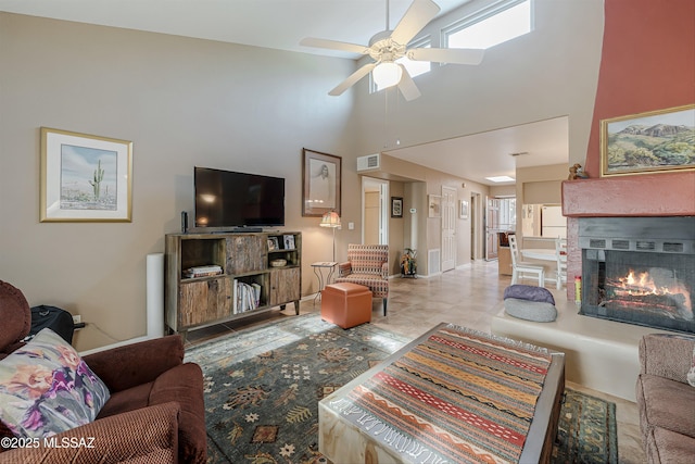 living room featuring a lit fireplace, visible vents, ceiling fan, and a towering ceiling