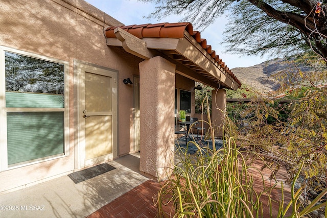 view of exterior entry featuring a mountain view, a tiled roof, and stucco siding