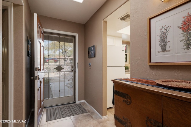 doorway to outside featuring light tile patterned floors, baseboards, visible vents, and a textured wall