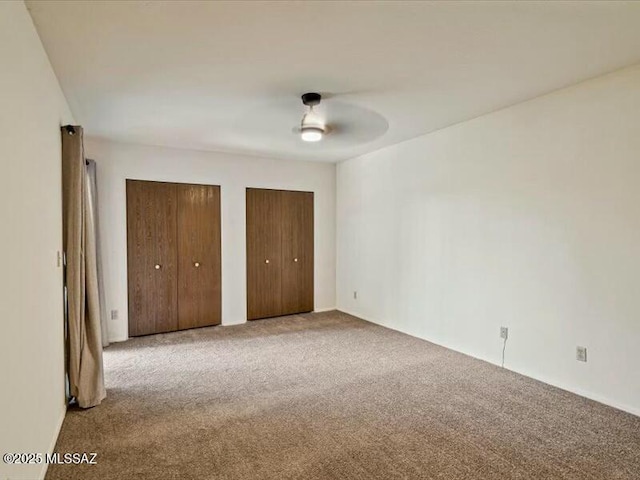 unfurnished bedroom featuring two closets, light colored carpet, and ceiling fan