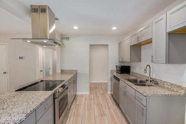 kitchen with appliances with stainless steel finishes, island range hood, sink, gray cabinetry, and light stone counters