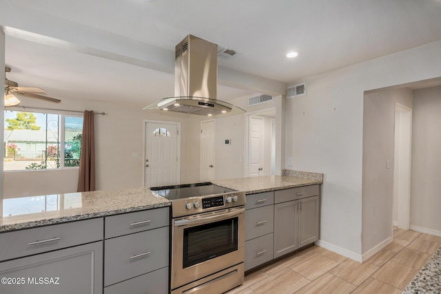 kitchen featuring gray cabinets, stainless steel range with electric stovetop, island exhaust hood, ceiling fan, and light stone countertops