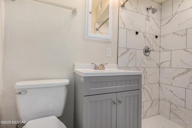 bathroom featuring vanity, a tile shower, and toilet