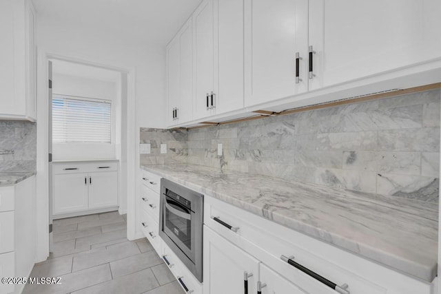 kitchen featuring white cabinetry, light stone countertops, light tile patterned flooring, and decorative backsplash