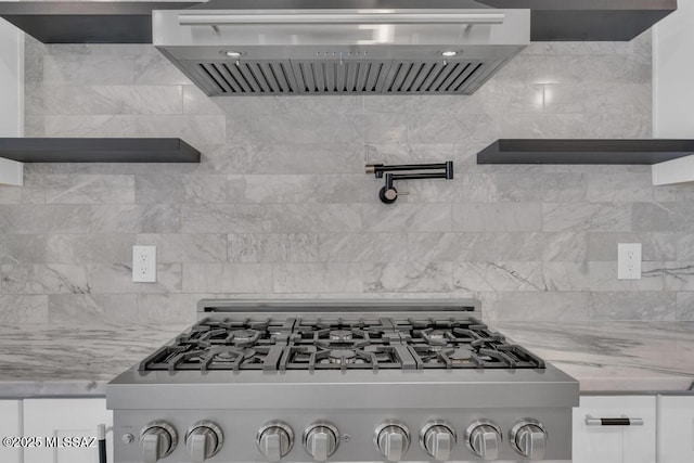 kitchen with white cabinetry, stainless steel gas range, light stone countertops, and wall chimney exhaust hood