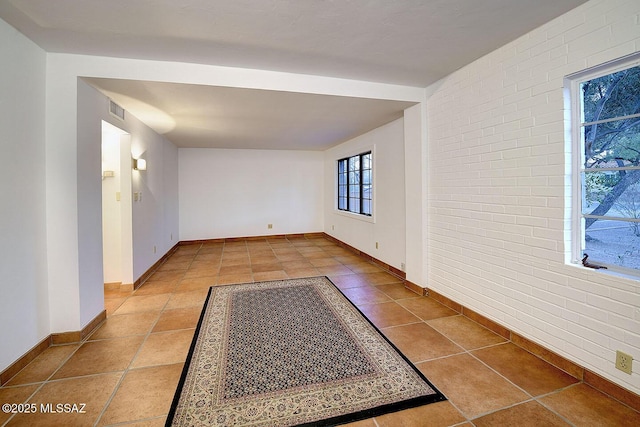 tiled spare room with brick wall, visible vents, and baseboards