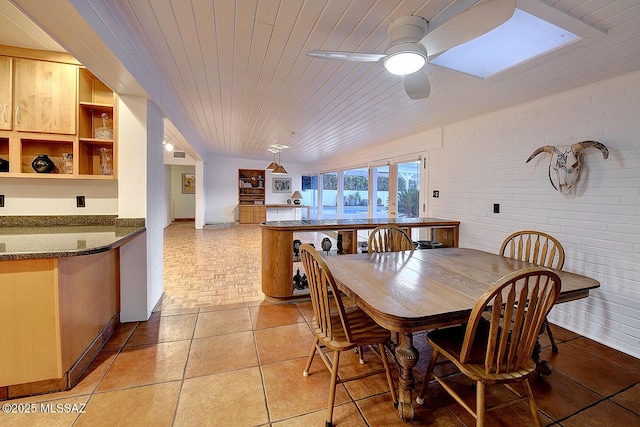 dining area with wood ceiling, a skylight, brick wall, and light tile patterned floors