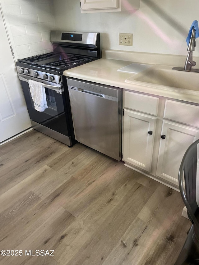 kitchen with light countertops, light wood-style floors, appliances with stainless steel finishes, and a sink