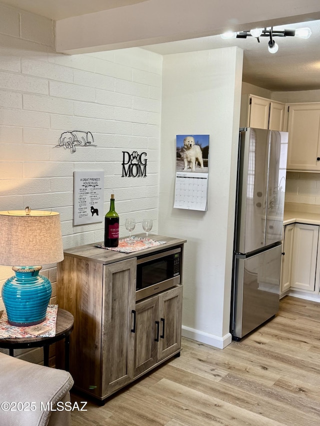 kitchen featuring brick wall, light wood finished floors, and appliances with stainless steel finishes