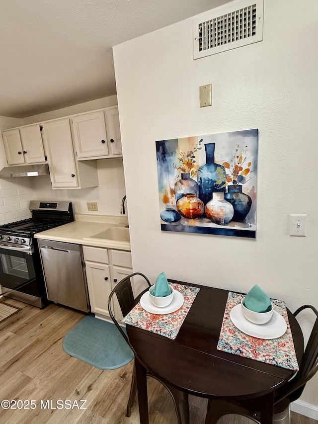 kitchen with visible vents, light wood finished floors, a sink, stainless steel appliances, and white cabinets