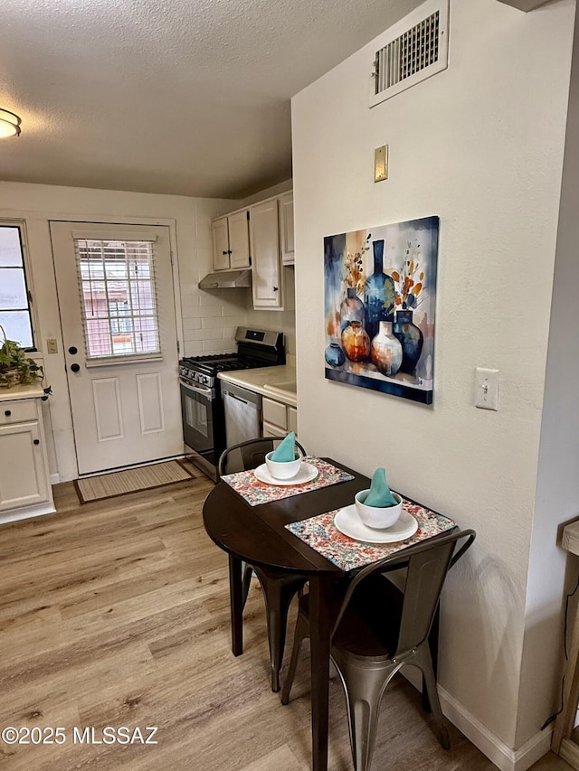 dining area with baseboards, light wood-style floors, visible vents, and a textured ceiling