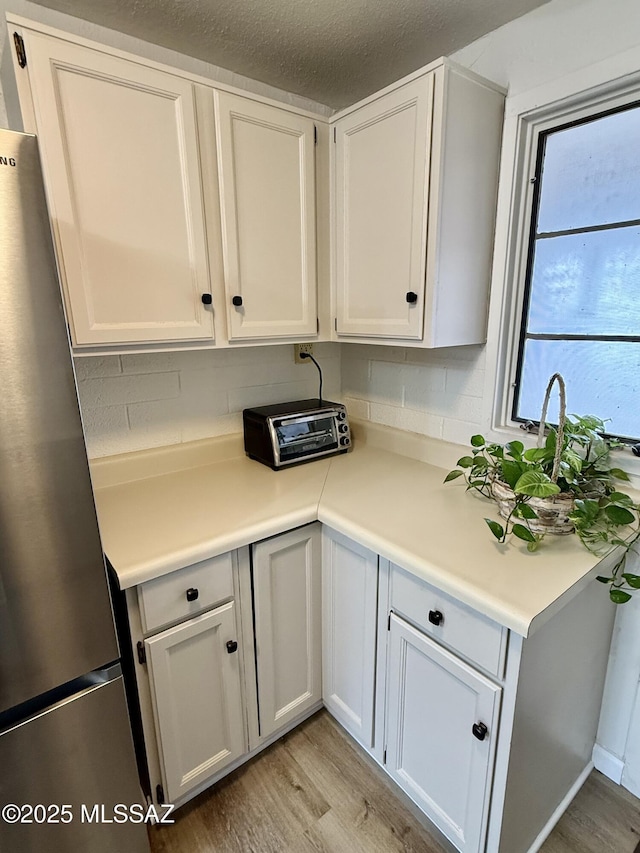 kitchen with light wood finished floors, white cabinets, tasteful backsplash, and freestanding refrigerator