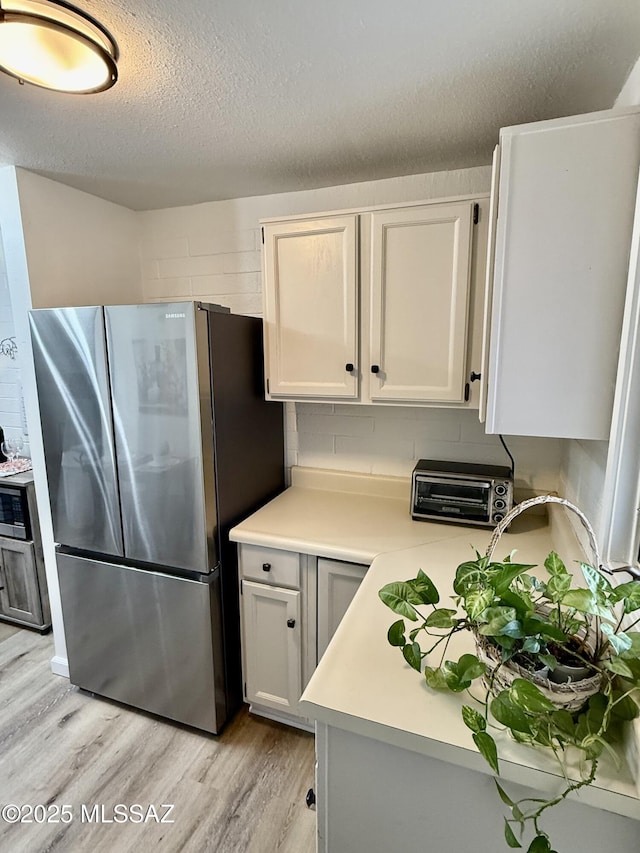 kitchen featuring a toaster, freestanding refrigerator, light countertops, a textured ceiling, and light wood-type flooring