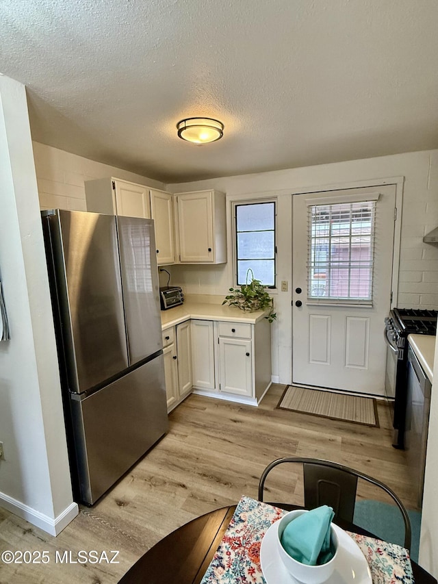 kitchen with freestanding refrigerator, light countertops, white cabinets, gas range, and light wood-type flooring