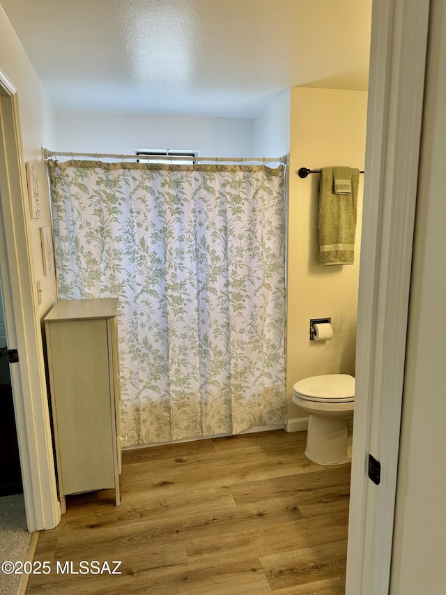 bathroom with curtained shower, toilet, and wood finished floors