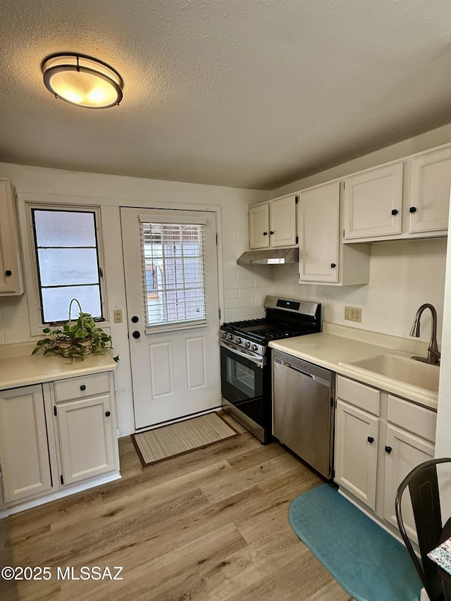 kitchen featuring light wood-style flooring, under cabinet range hood, a sink, white cabinetry, and stainless steel appliances