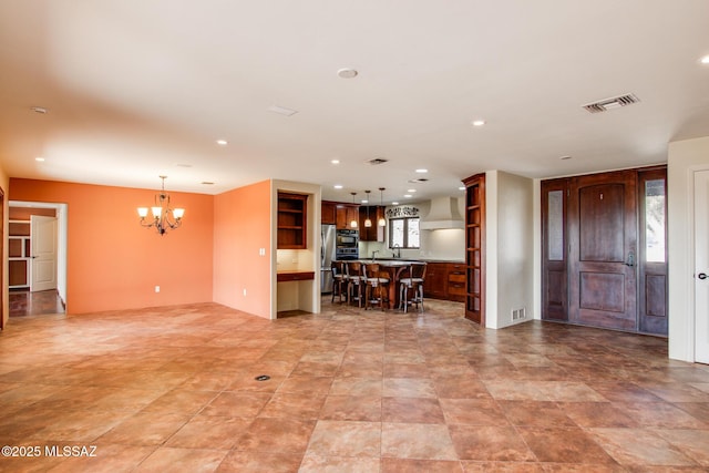 kitchen with stainless steel refrigerator, decorative light fixtures, a breakfast bar area, and wall chimney range hood