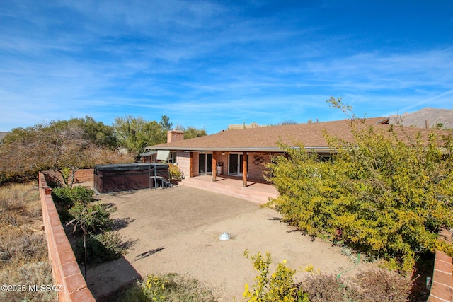 rear view of house with a mountain view, a hot tub, and a patio