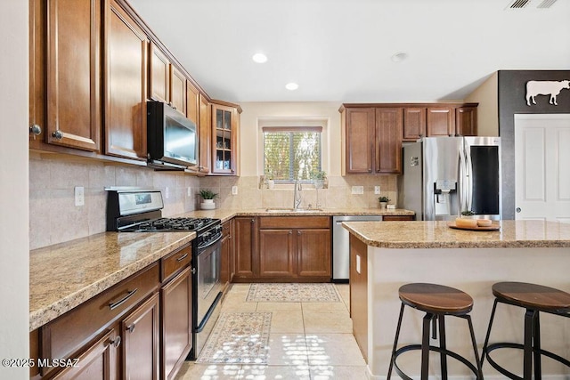 kitchen with sink, light tile patterned floors, backsplash, stainless steel appliances, and a kitchen breakfast bar