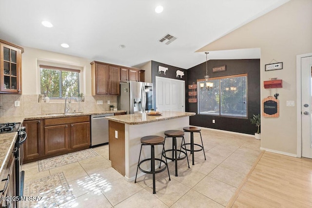 kitchen with lofted ceiling, sink, hanging light fixtures, stainless steel appliances, and a center island