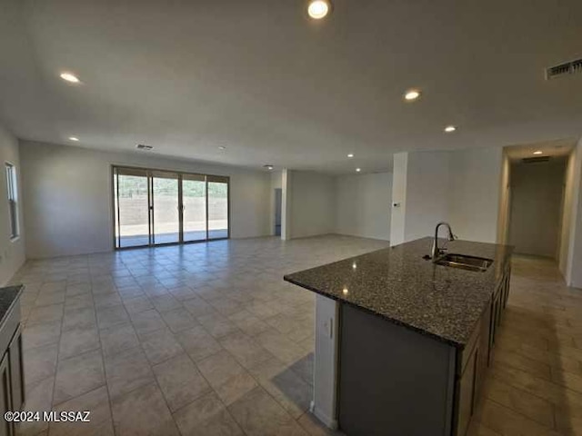 kitchen with a kitchen island with sink, sink, and dark stone countertops