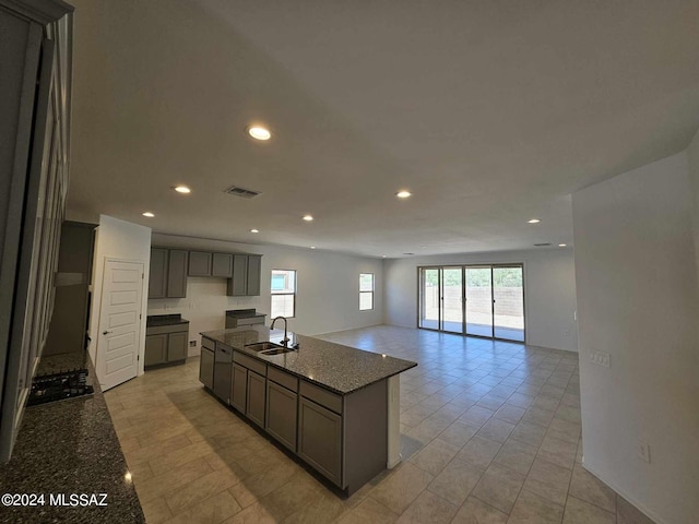 kitchen with an island with sink, sink, light tile patterned floors, and dark stone counters