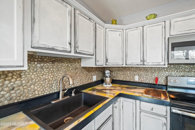 kitchen with vaulted ceiling, appliances with stainless steel finishes, sink, white cabinets, and backsplash