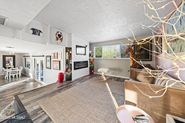 living room featuring wood-type flooring, a stone fireplace, and plenty of natural light