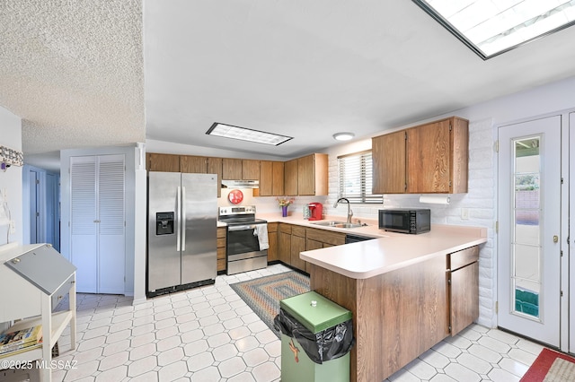 kitchen featuring stainless steel appliances, sink, a textured ceiling, and kitchen peninsula