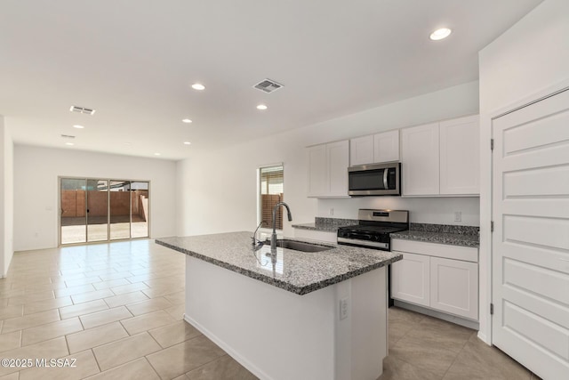 kitchen with appliances with stainless steel finishes, sink, dark stone countertops, white cabinets, and a center island with sink