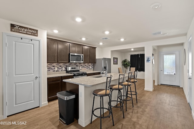 kitchen featuring appliances with stainless steel finishes, a kitchen island with sink, dark brown cabinetry, and light hardwood / wood-style flooring