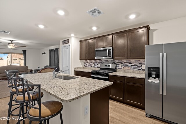 kitchen with stainless steel appliances, an island with sink, dark brown cabinetry, and light hardwood / wood-style flooring