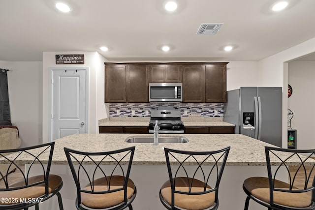 kitchen featuring tasteful backsplash, stainless steel appliances, an island with sink, and dark brown cabinets