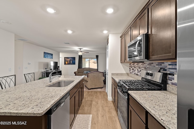 kitchen with appliances with stainless steel finishes, an island with sink, sink, backsplash, and light wood-type flooring