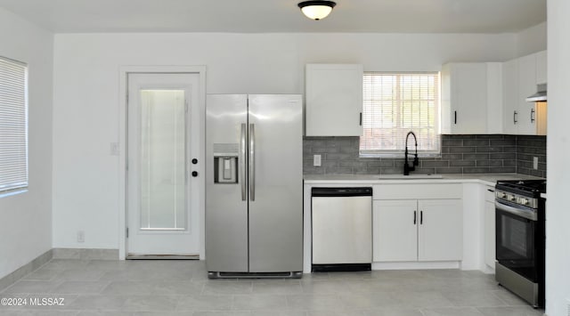 kitchen with appliances with stainless steel finishes, tasteful backsplash, sink, white cabinets, and wall chimney exhaust hood