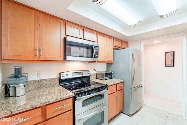 kitchen with a toaster, light tile patterned floors, stainless steel appliances, light stone countertops, and baseboards