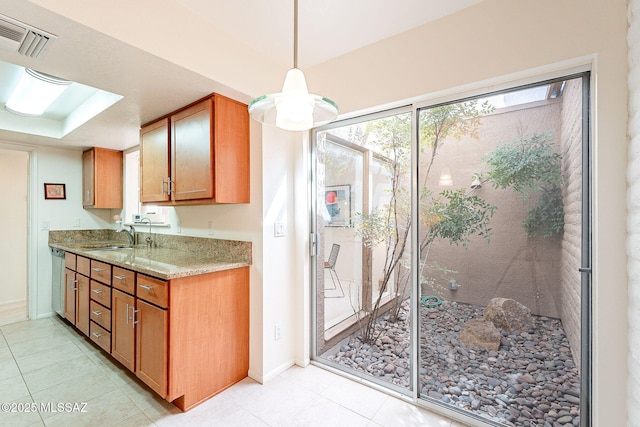 kitchen featuring light stone countertops, visible vents, brown cabinetry, and a sink