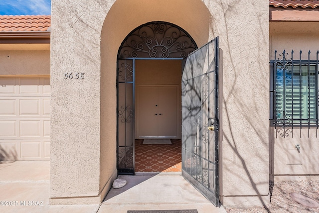 view of exterior entry featuring a tiled roof, an attached garage, and stucco siding