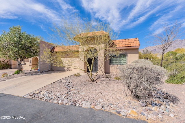 view of front of home featuring driveway, an attached garage, a tile roof, and stucco siding