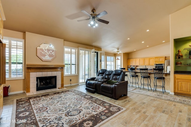 living room with ceiling fan, light wood-type flooring, a tiled fireplace, and lofted ceiling