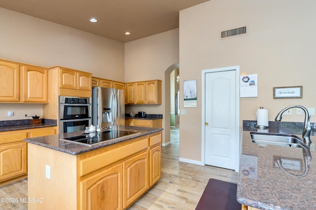 kitchen featuring a center island, sink, a high ceiling, dark stone counters, and appliances with stainless steel finishes