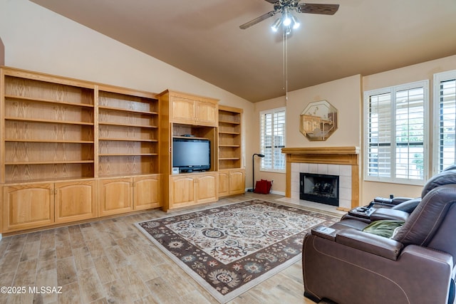 living room with a tile fireplace, light wood-type flooring, vaulted ceiling, and ceiling fan