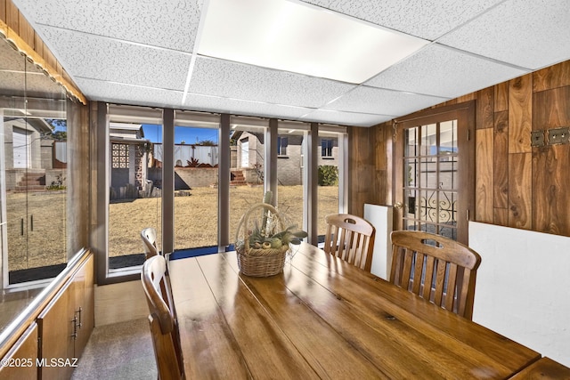 dining space featuring a drop ceiling and wooden walls