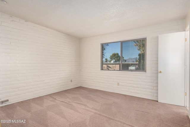 carpeted empty room with a textured ceiling and brick wall