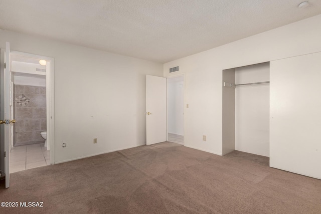 unfurnished bedroom with ensuite bathroom, light colored carpet, a textured ceiling, and a closet