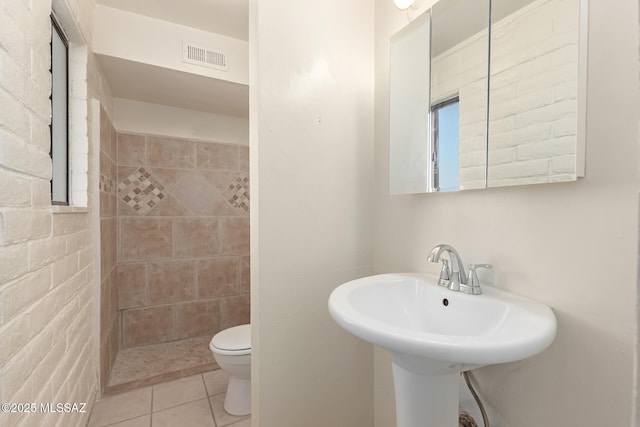 bathroom with tiled shower, tile patterned floors, toilet, and sink