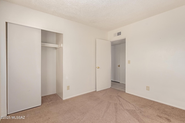 unfurnished bedroom featuring light colored carpet, a closet, and a textured ceiling