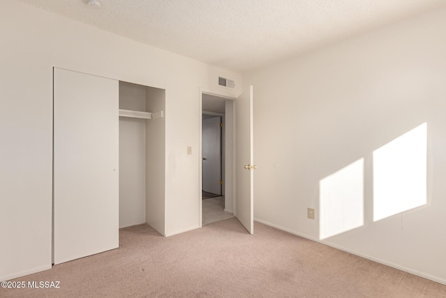 unfurnished bedroom with light colored carpet, a closet, and a textured ceiling