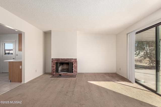 unfurnished living room with a brick fireplace, light colored carpet, and a textured ceiling