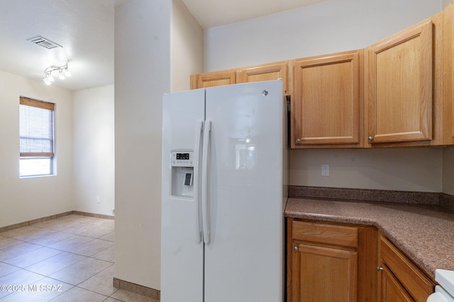 kitchen with light tile patterned floors, white fridge with ice dispenser, visible vents, and baseboards